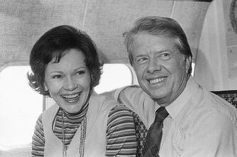 A black-and-white photo of former U.S. President Jimmy Carter and his wife Rosalynn Carter smiling together inside an…