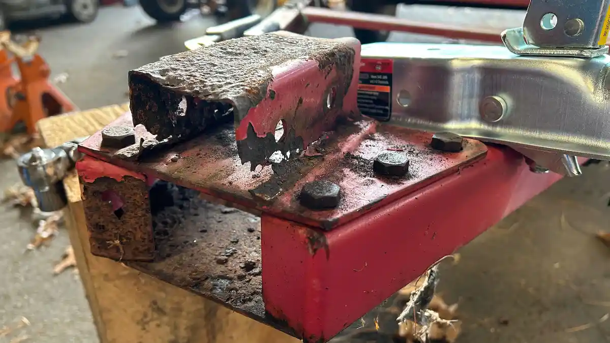 A close-up photo shows a red metal trailer hitch with severe rust damage, especially on the top mounting plate where the…