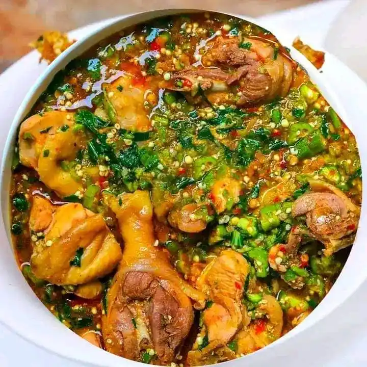 a close-up photo of a white bowl filled with cooked chicken pieces submerged in a rich, oily sauce generously topped with…