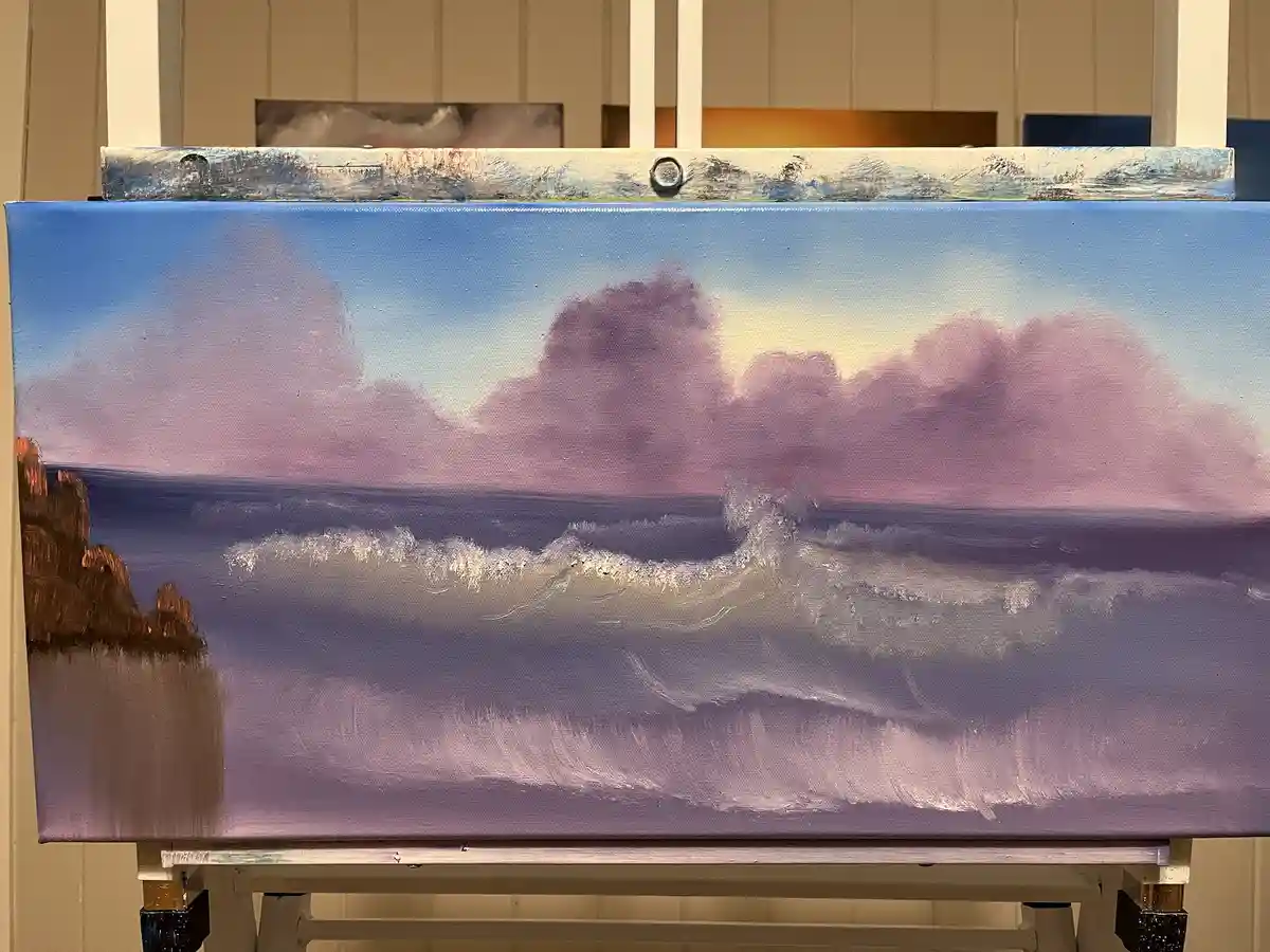A painting of a serene ocean scene with purple and blue clouds and waves on an easel, overlaid with the text 'i'm not lazy…