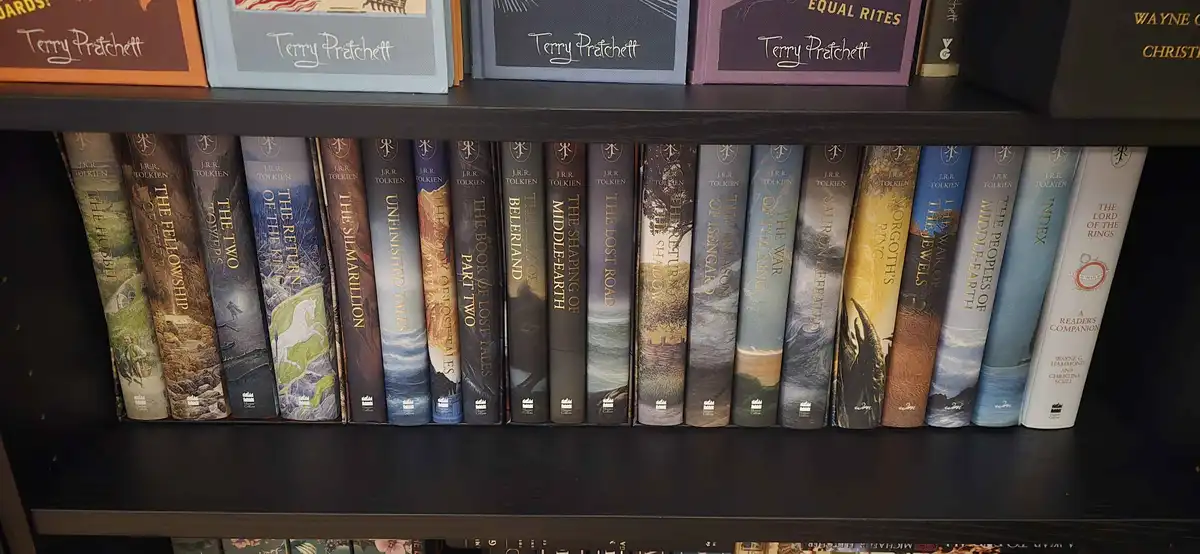 A close-up of a dark wooden bookshelf showing a row of J.R.R. Tolkien books, including 'The Hobbit', 'The Fellowship of the…