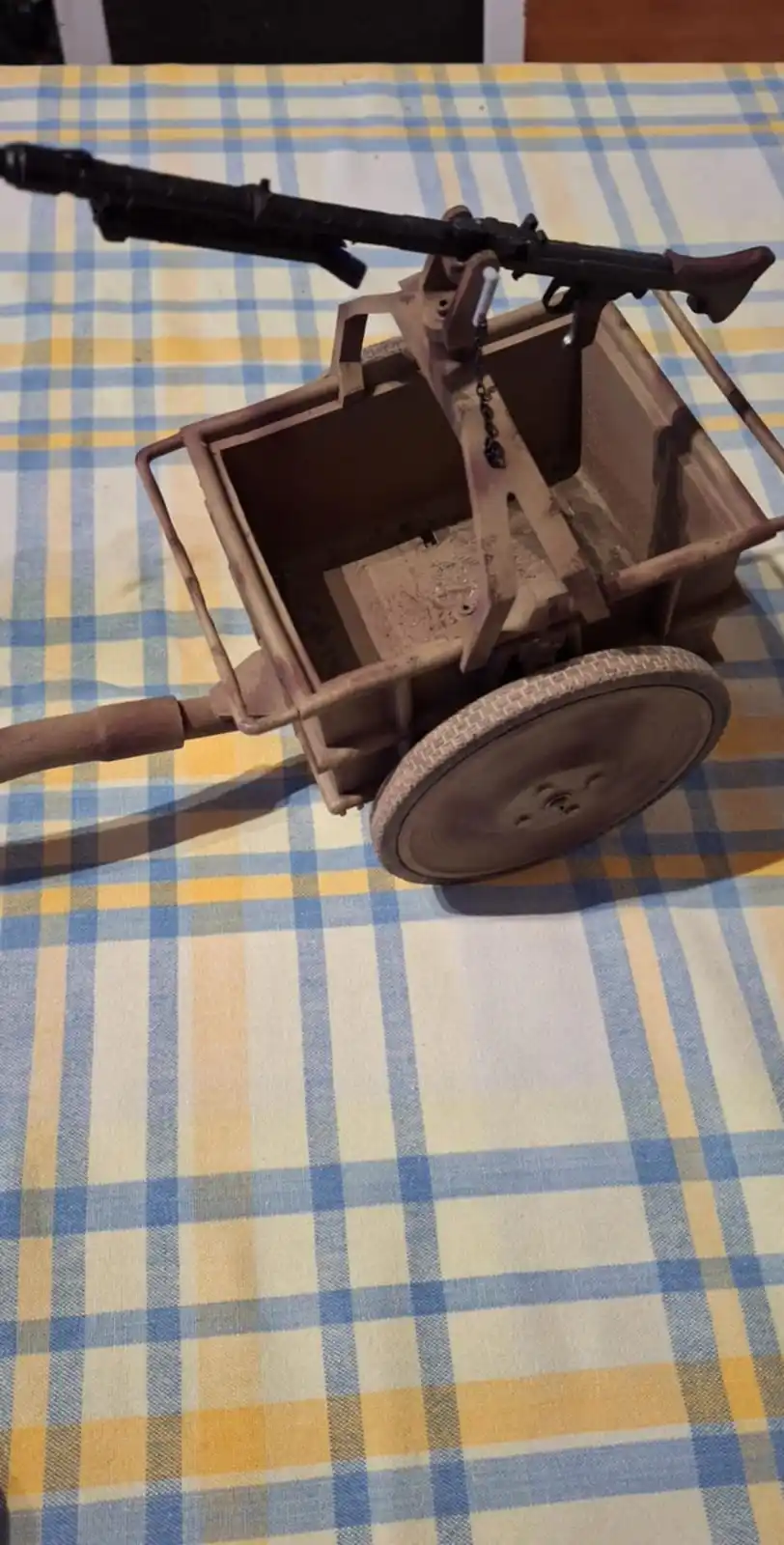 A handmade model of a World War II German machine gun mounted on a wooden shopping cart with a single wheel, placed on a…