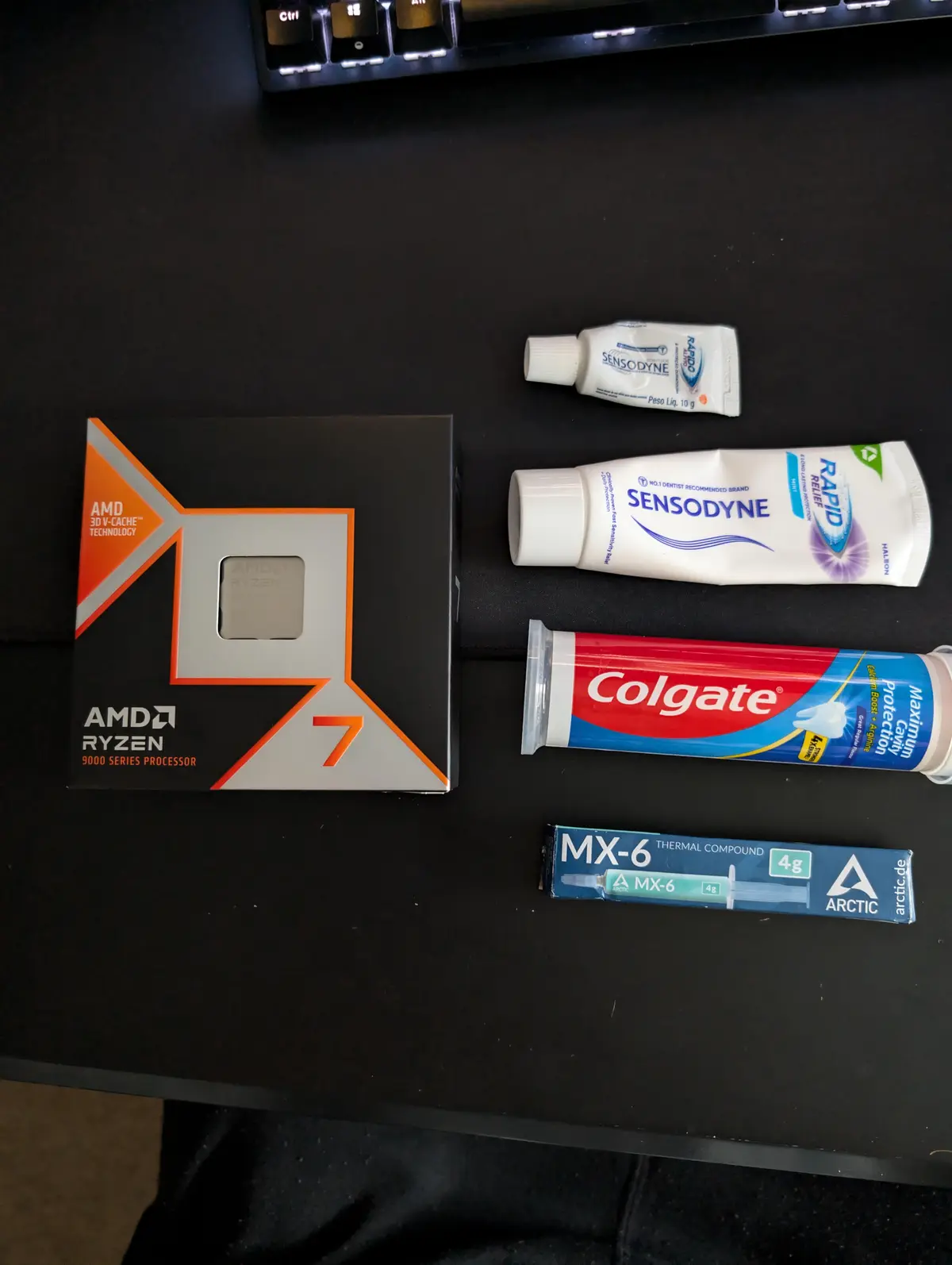 An overhead shot displays an AMD Ryzen 9000 Series processor box, two tubes of toothpaste (Sensodyne and Colgate), and a…