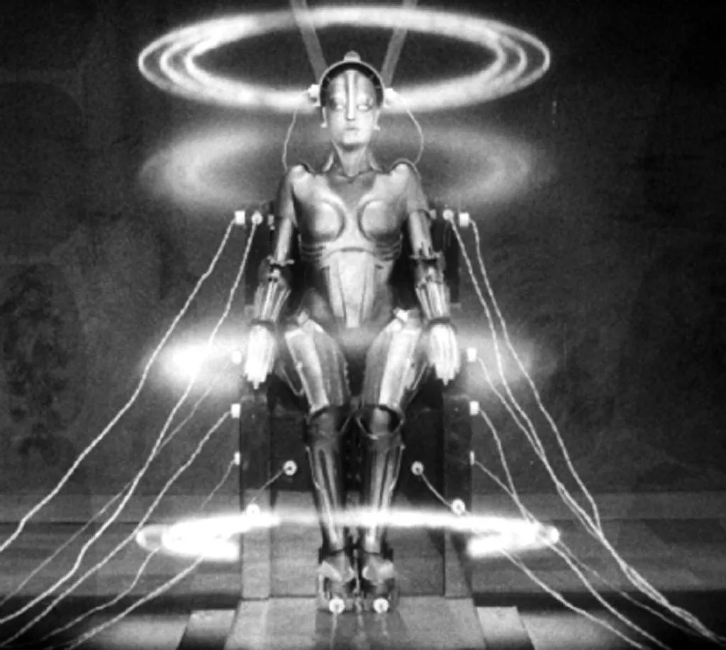 A black-and-white image shows a humanoid robot seated in a chair, surrounded by glowing circular lights and wires connected…