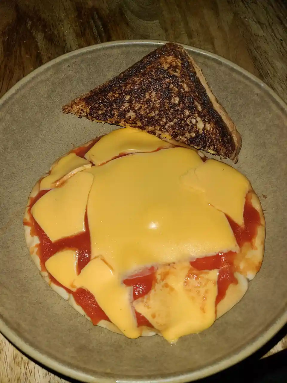 A plate holds a round, flatbread-like base topped with tomato sauce and melted cheese, alongside a triangular piece of…