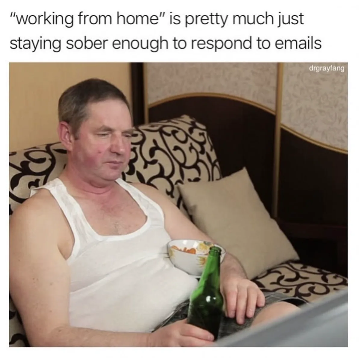 A man in a white tank top sits on a patterned couch holding a green beer bottle and a bowl of snacks, looking drowsy and…
