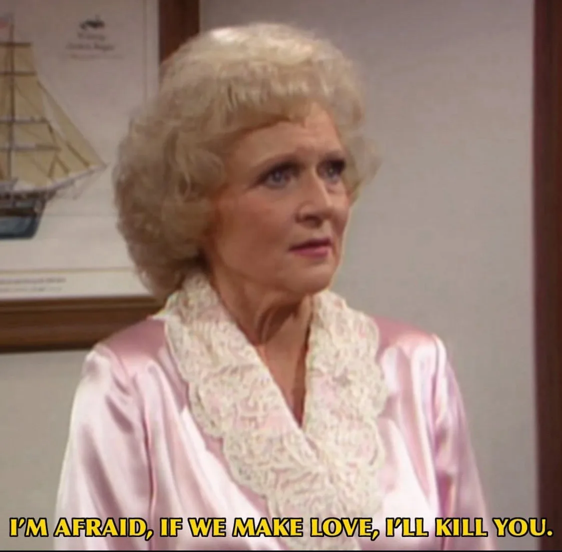 A still image of actress Betty White, portraying her character from 'The Golden Girls,' wearing a pink satin robe with a…