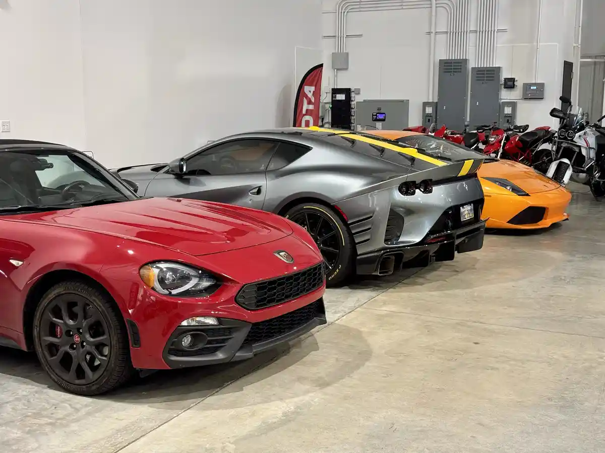 A row of luxury sports cars, including a red Ferrari, a silver Ferrari, and an orange Lamborghini, are parked in a clean…