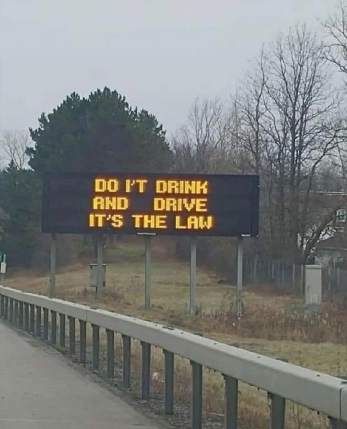 A roadside electronic sign displays the message 'DO I'T DRINK AND DRIVE IT'S THE LAW' in bright yellow letters, with a typo…
