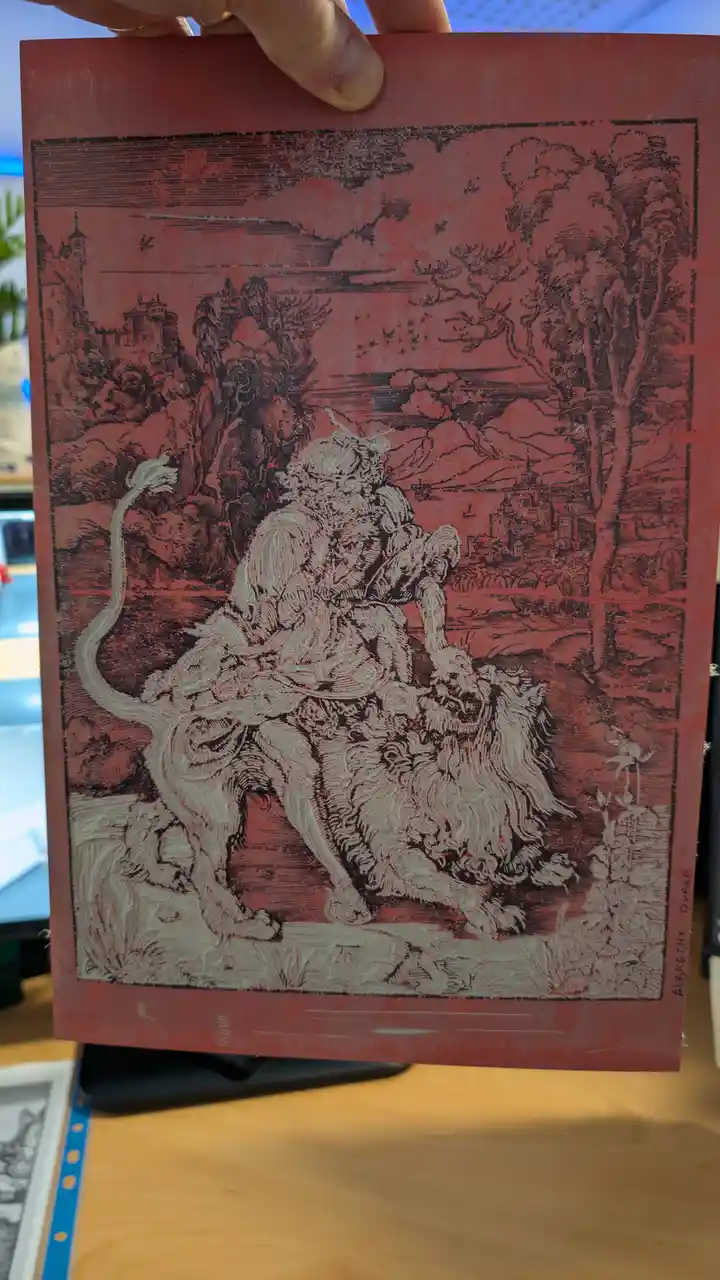 A hand holds up a red-toned print of Albrecht Dürer's 'Knight, Death and the Devil,' showing a knight on horseback with a…
