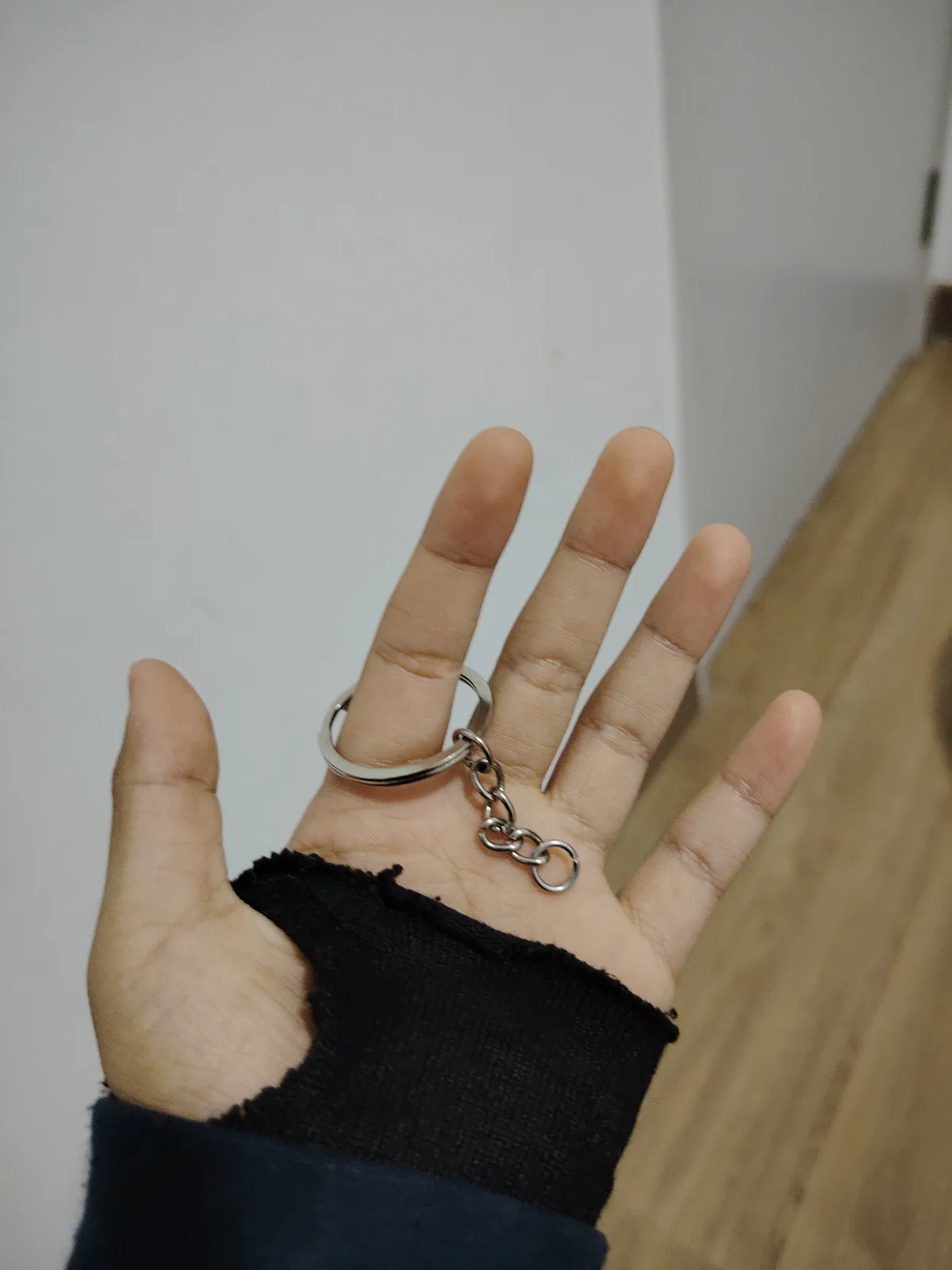 A person's open hand, wearing a black fingerless glove, has a silver keychain ring slipped onto the middle finger. The…