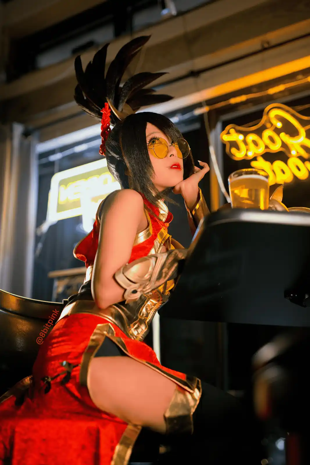 A person in a detailed cosplay of a character with black hair, a red and gold outfit, and a feathered headpiece sits at a…