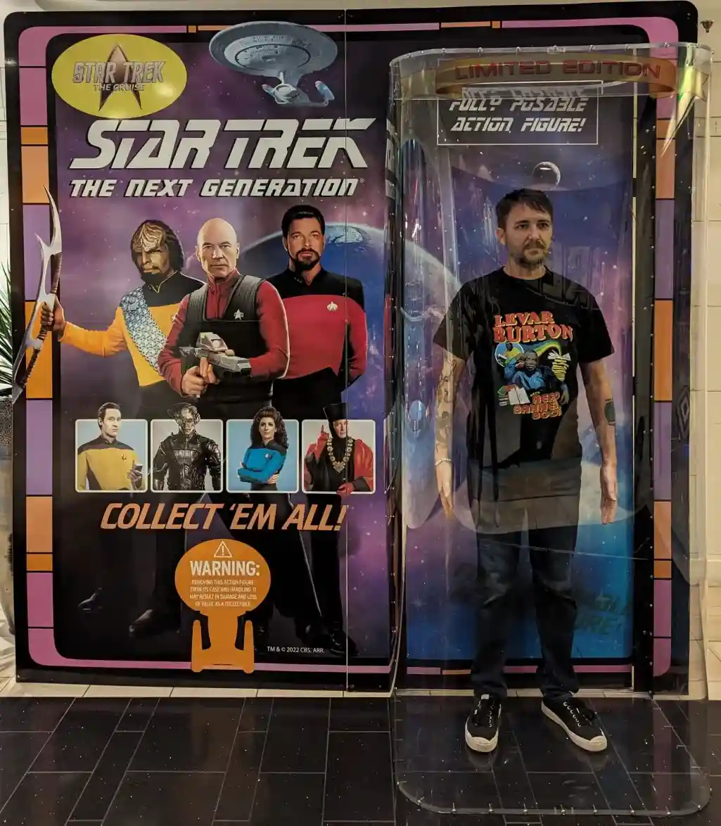 A man stands inside a clear plastic display case labeled 'LIMITED EDITION FULLY POSABLE ACTION FIGURE!' next to a 'Star…