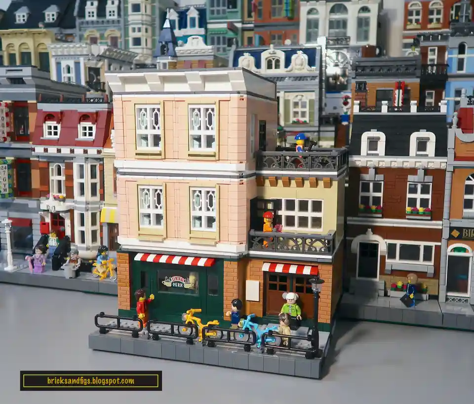 A detailed LEGO diorama of a city street features a central building with a green storefront and red-and-white striped…