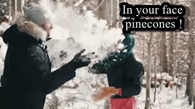 Two people stand in a snowy forest, one wearing a grey beanie and black coat with fur trim, the other wearing a green beanie…
