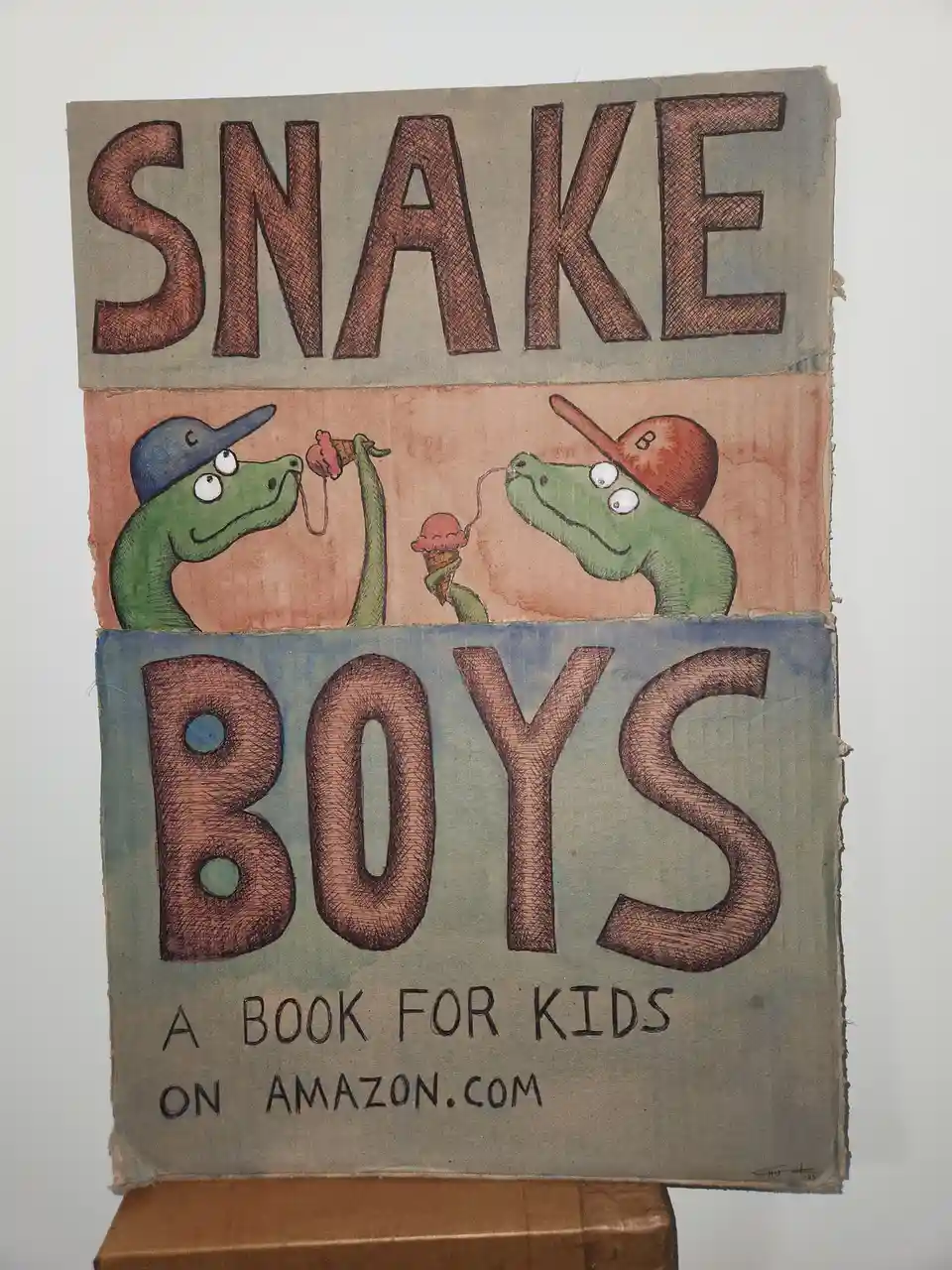 The image shows a handmade book cover with the title 'SNAKE BOYS' in large, textured letters. Below the title, two…