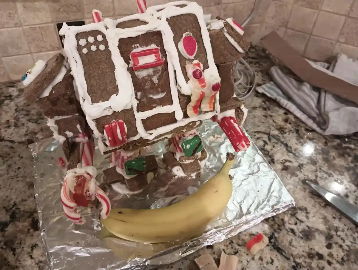 A gingerbread house made of brown cookies and white icing, decorated with candy canes and other sweets, sits on aluminum…