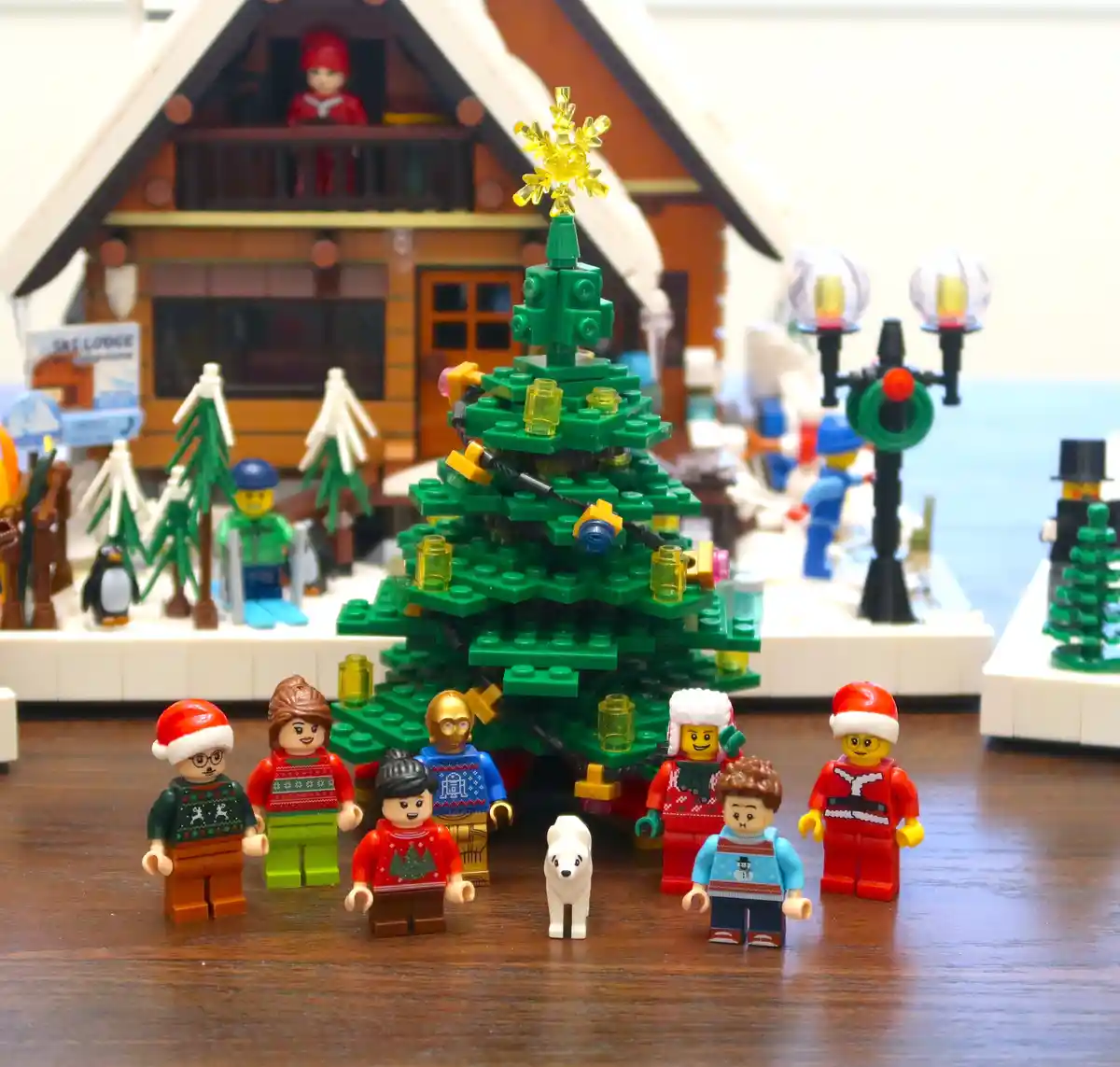 A festive Lego Christmas scene features a large green Lego tree adorned with yellow lights and a snowflake topper…