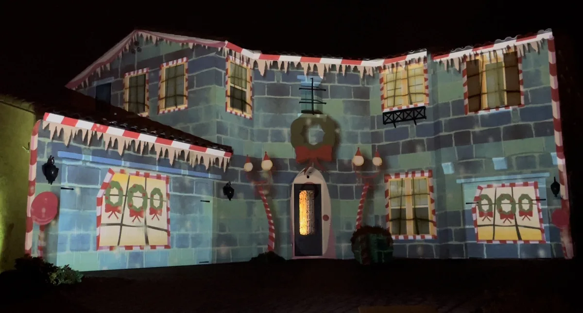 A house at night is covered in a projected cartoonish Christmas decoration, featuring candy cane trim, icicles, wreaths, and…