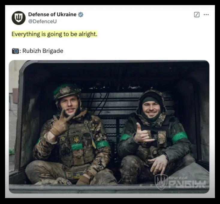 Two Ukrainian soldiers in camouflage gear and helmets sit inside a military vehicle, both smiling and giving thumbs-up…