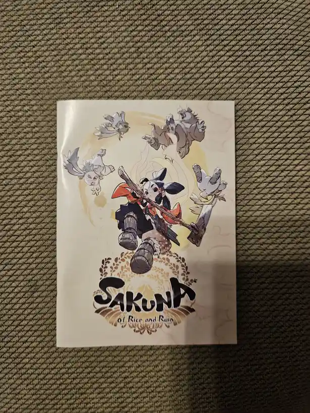 A printed promotional image for the video game 'Sakuna of Rice and Rain' shows the main character, Sakuna, in traditional…