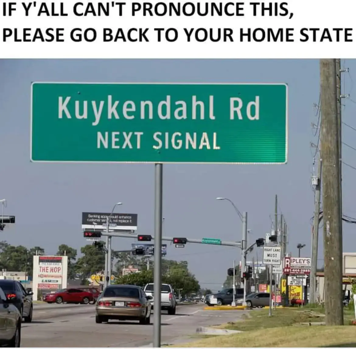 A green road sign reads 'Kuykendahl Rd NEXT SIGNAL' above a street intersection with cars, traffic lights, and commercial…