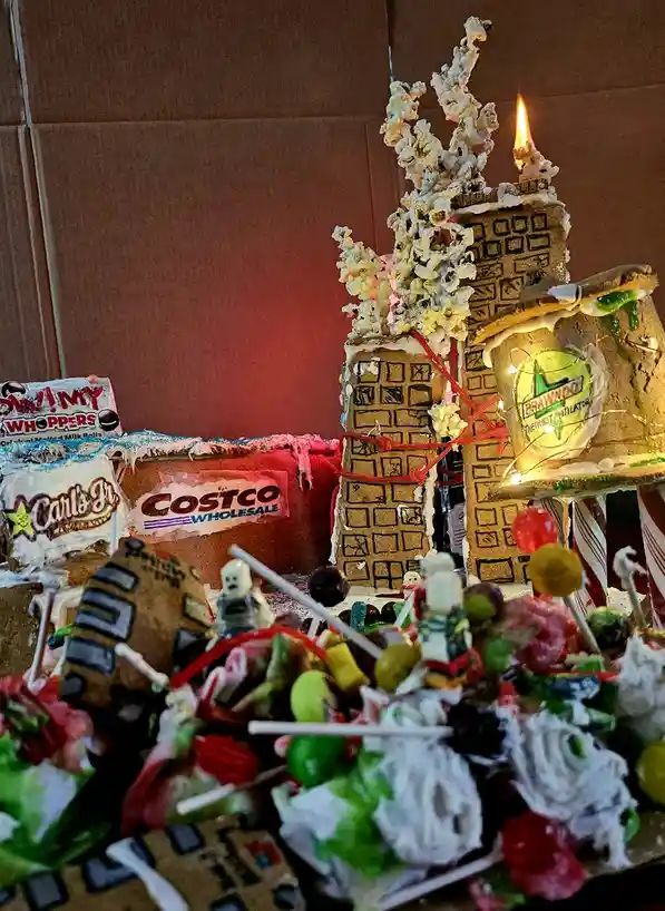 A chaotic, candy-covered gingerbread cityscape with buildings made of graham crackers and icing, topped with popcorn and a…