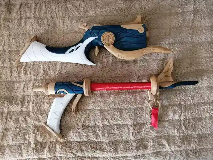 Two intricately crafted wooden toy guns with blue, white, and natural wood finishes lie on a textured beige blanket. The top…