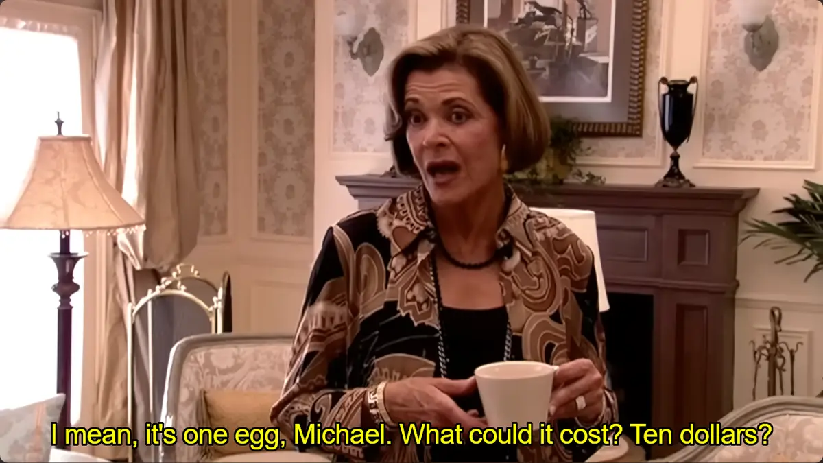 A woman with short brown hair, wearing a patterned blouse, sits in a luxurious room holding a white mug. She has a shocked…