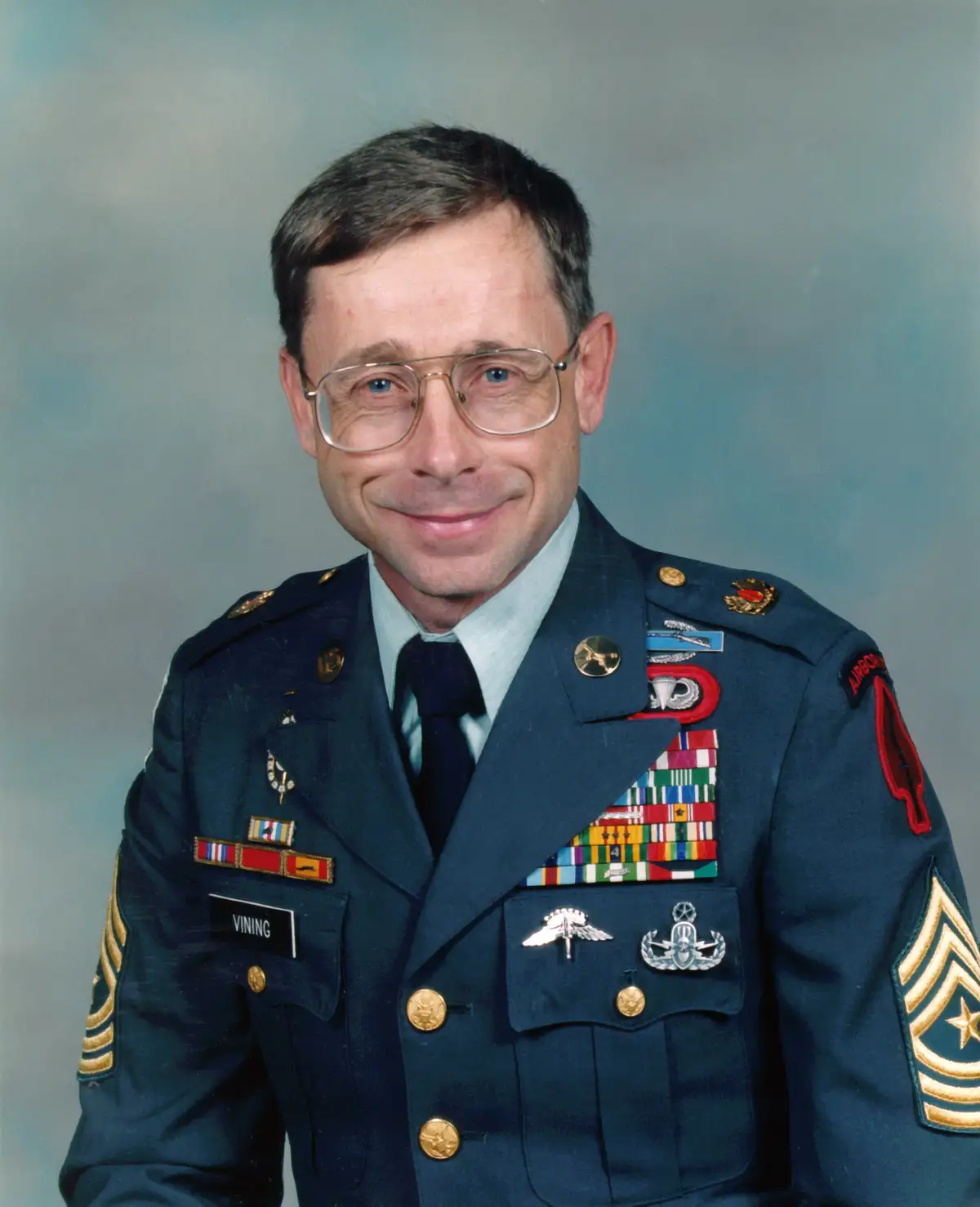 A formal military portrait of a man in a dark blue uniform adorned with numerous medals, ribbons, and insignia, including an…