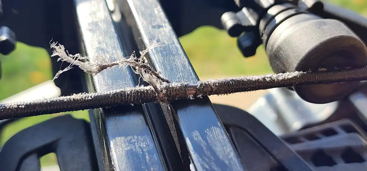 A close-up photo shows a frayed, worn black cable with shredded insulation resting on a black metal frame, likely part of a…