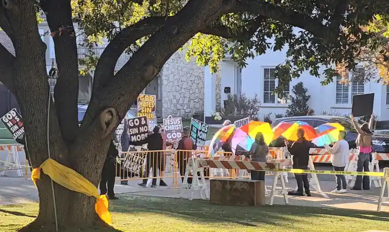 A group of people holding religious protest signs like 'GOD HATES SIN SINNERS' and 'JESUS CHRIST IS GOD' stand across a…