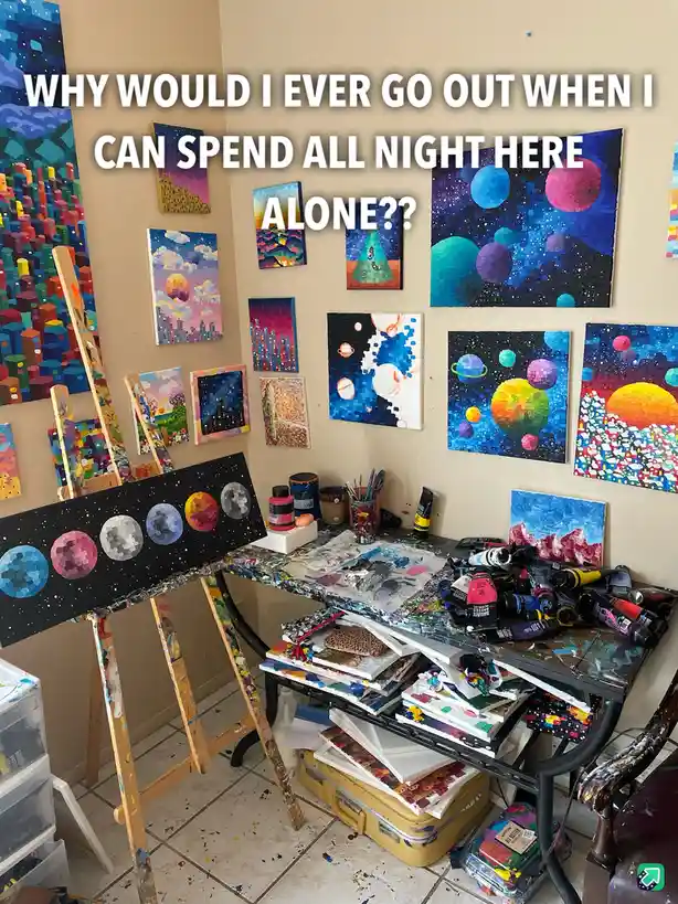 A cluttered artist's studio filled with colorful pixelated paintings on easels and walls, paint tubes, brushes, and canvases…