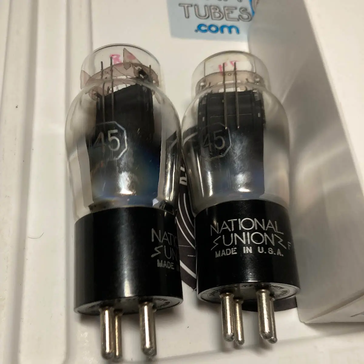 Two vintage glass vacuum tubes with black bases labeled 'NATIONAL UNION MADE IN U.S.A.' and '45' inside, sitting side by…
