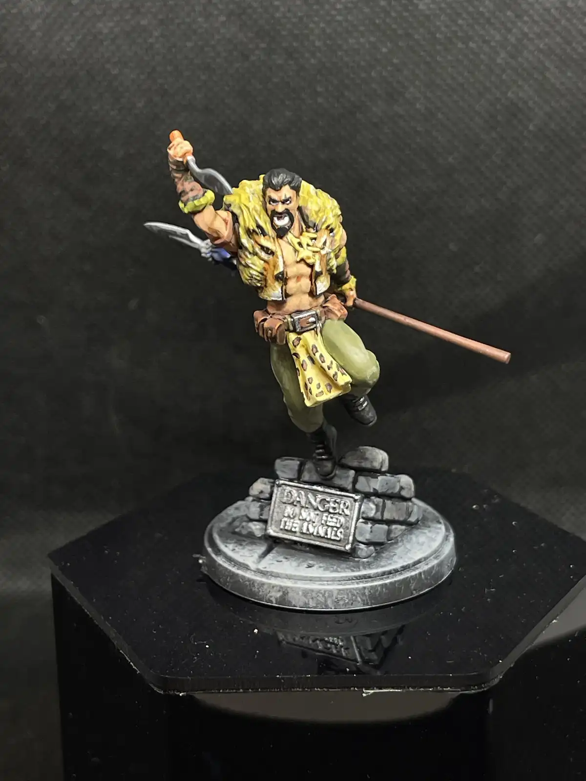A painted miniature figurine of a muscular, bearded warrior in a yellow leopard-print vest and green pants, wielding a sword…