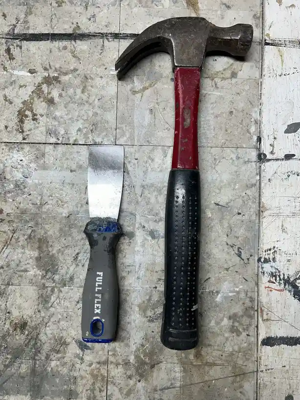 A well-worn claw hammer with a red handle and black grip lies next to a smaller putty knife with a gray handle labeled 'FULL…