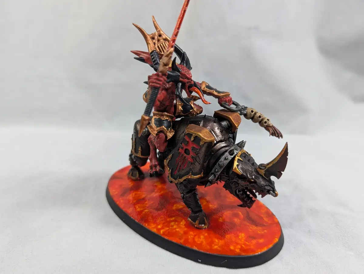 A highly detailed, painted miniature of a demonic rider on a heavily armored, horned beast, both adorned in red and gold…