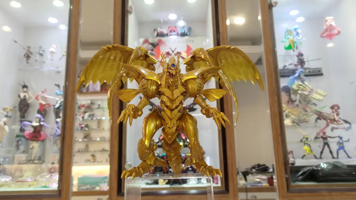A large, golden, robotic dragon figure with spread wings stands on a clear stand in front of glass display cases filled with…