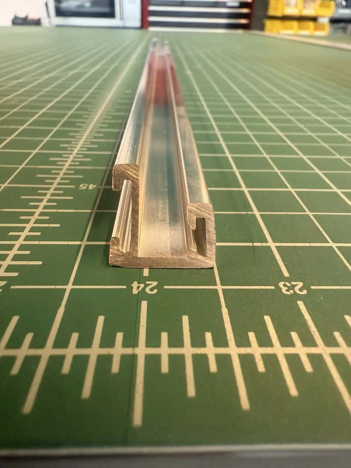 A long, metallic ruler with a U-shaped cross-section lies diagonally on a green cutting mat with grid lines and…