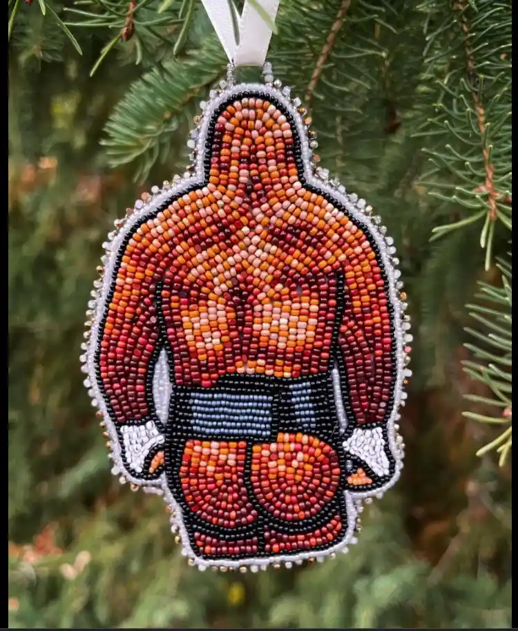 A beaded Christmas ornament shaped like a muscular boxer, hanging on a pine tree branch, with the text 'i'm not a boxer, i'm…