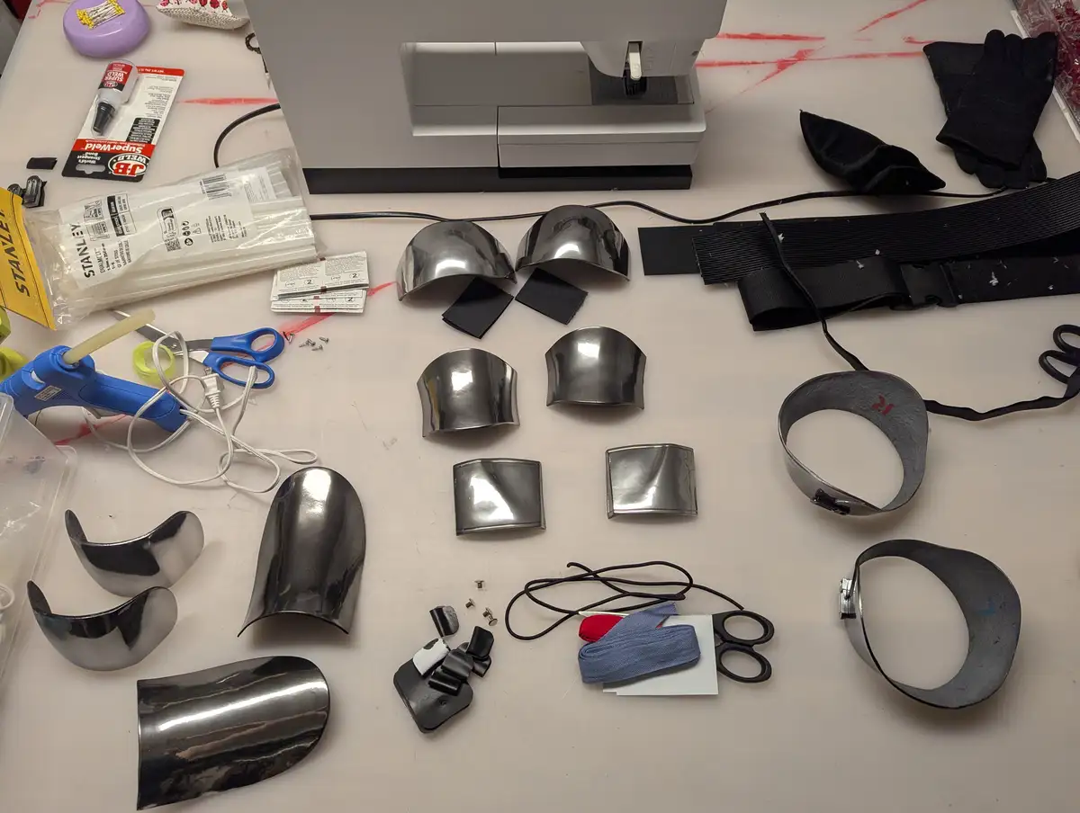 A cluttered workbench displays numerous shiny, chrome-plated armor pieces of various shapes and sizes, alongside crafting…