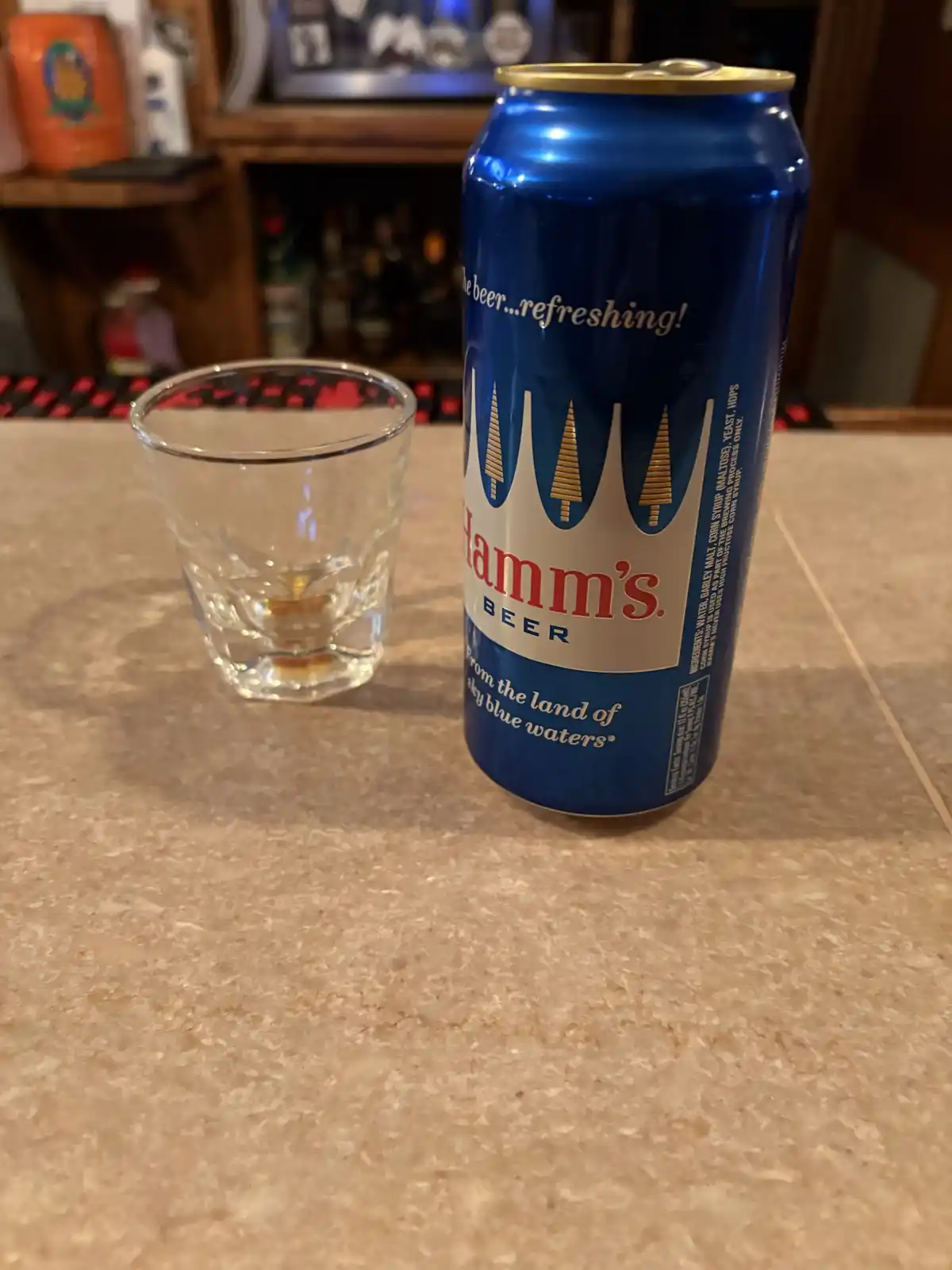 A blue Hamm's beer can sits next to an empty shot glass on a countertop, with the text 'the beer...refreshing!' overlaid on…
