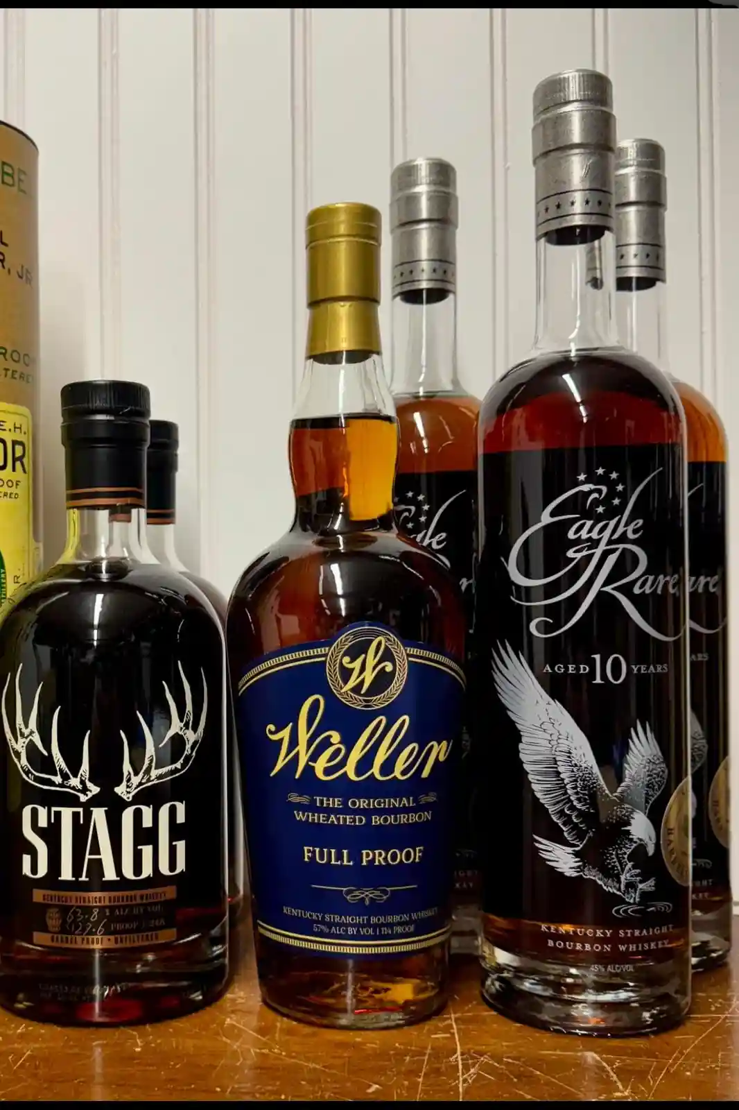 A collection of several bourbon whiskey bottles, including Stagg, Weller Full Proof, and Eagle Rare 10 Years, are arranged…