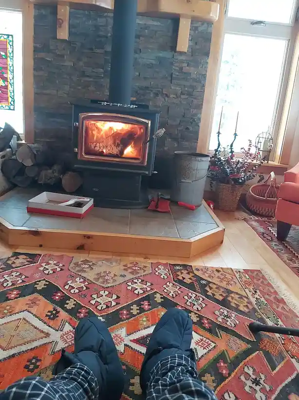 A first-person view shows someone's legs in plaid pajama pants and dark slippers resting on a colorful patterned rug in…