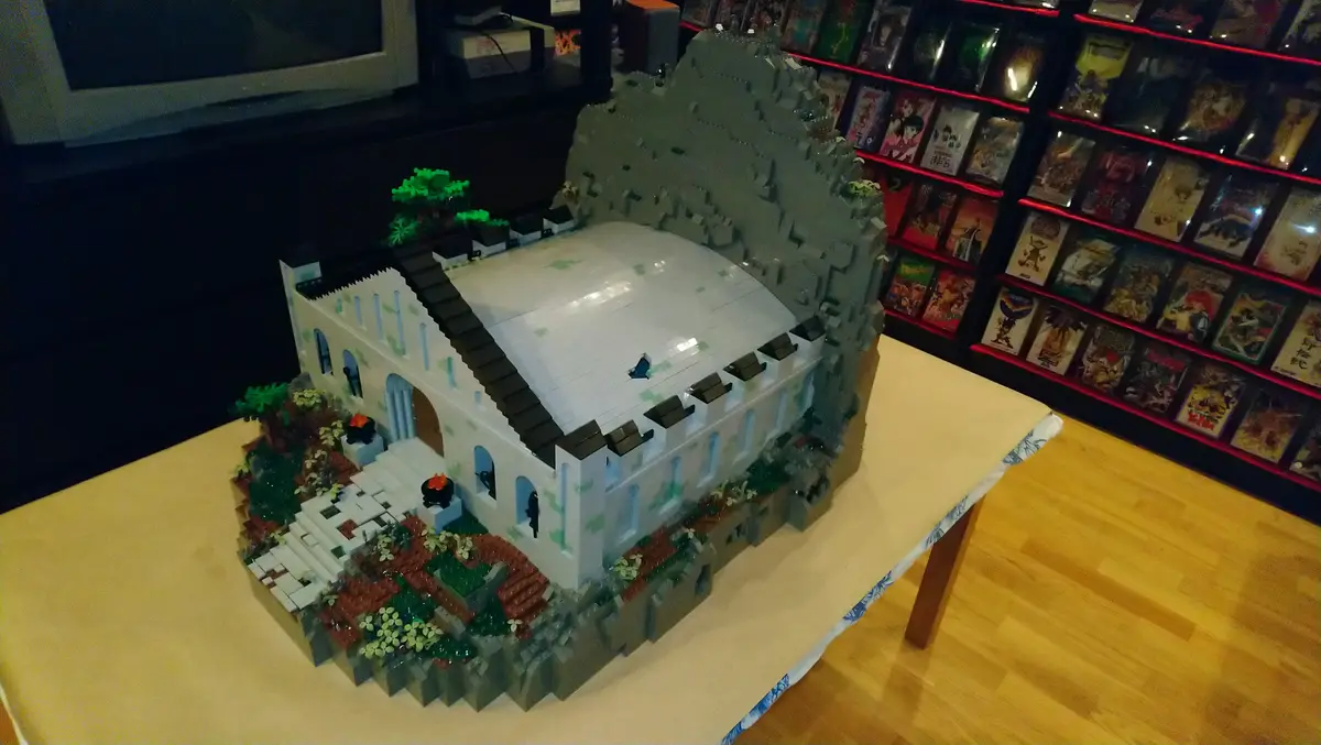 a detailed lego model of a castle with a large, empty courtyard, surrounded by gray stone walls and small green trees, sits…