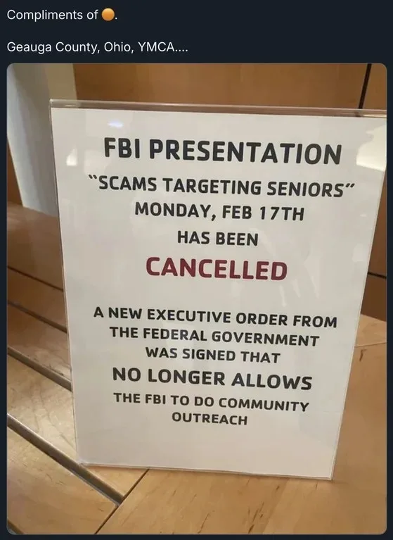 A white sign in a clear plastic holder on a wooden surface announces the cancellation of an 'FBI Presentation: Scams…