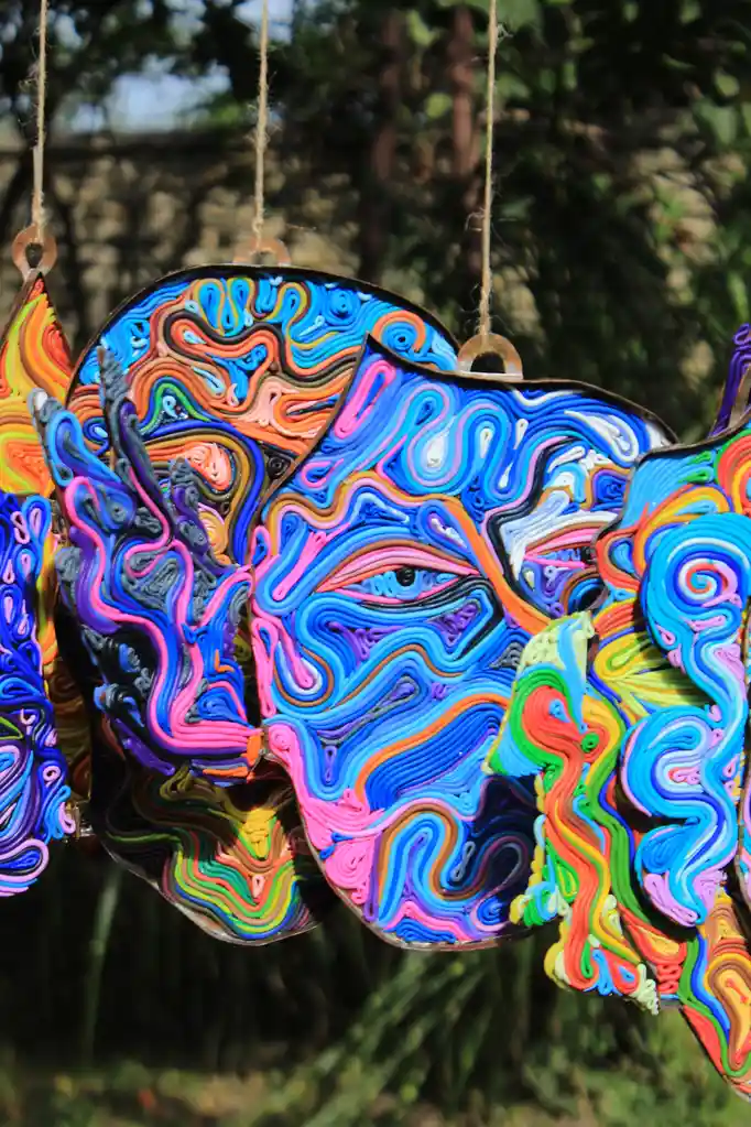 A vibrant, colorful quilled art piece shaped like a human face with swirling patterns and a single visible eye, hanging…