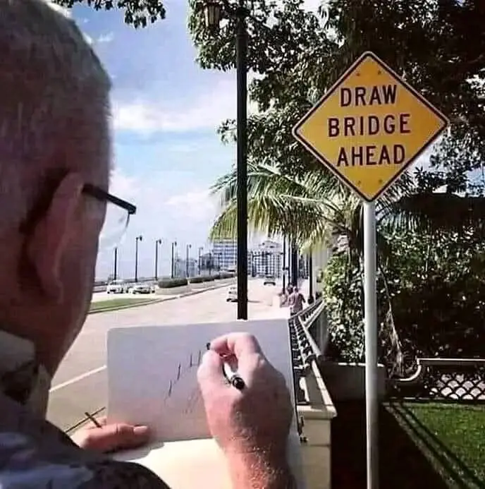 An older man with glasses is seen from behind, sketching on a notepad while standing near a yellow diamond-shaped road sign…