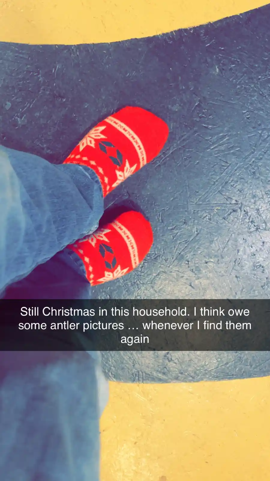 A close-up photo shows a person's feet wearing bright red, patterned Christmas socks with white and dark blue snowflake…