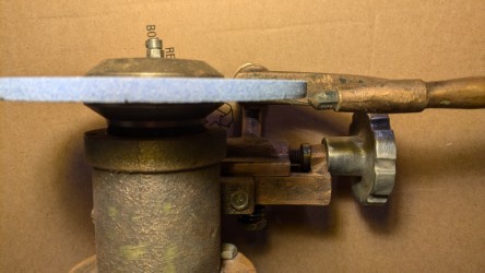 a close-up photo of a vintage, rusty metal grinding wheel with a blue abrasive disc, mounted on a wooden and metal stand…
